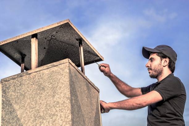 a professional carpenter man is installing a typical exhaust chimney for ventilation heavy system of kitchens  made by an aluminum at roof top and wearing blue uniform and cap